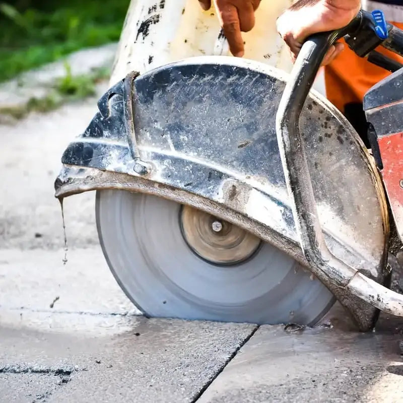Close-up of a walk-behind concrete cut-off saw with a diamond blade performing a wet cut on asphalt.