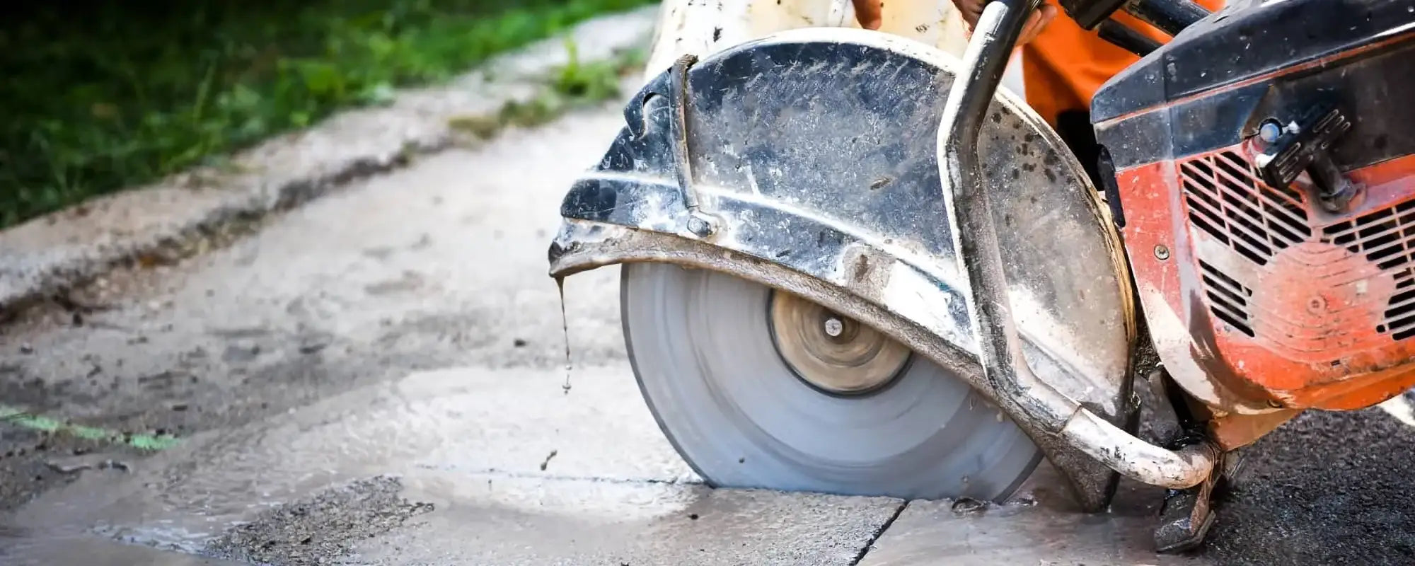 Close-up of a walk-behind concrete cut-off saw with a diamond blade performing a wet cut on asphalt.